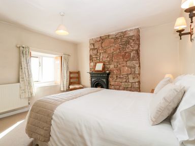 A bedroom with a bed pillows a stone fireplace a wooden chair and floral curtains at Gordons View Pleasant Stile near Gloucester