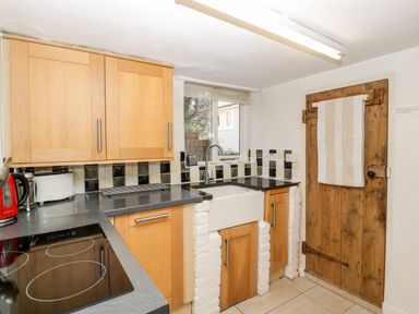 A kitchen with wooden cabinets black countertop a sink below a small window and a wooden door with a towel at Gordons View Pleasant Stile near Gloucester