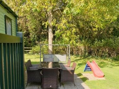a garden area with a table and chairs near a tree and a small slide at Hafan y Mor Haven - Holiday Accommodation 11370 in Pwllheli