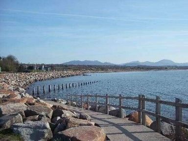 a coastal scene with a pathway along the shore and mountains in the distance at Hafan y Mor Haven - Holiday Accommodation 11370 Pwllheli