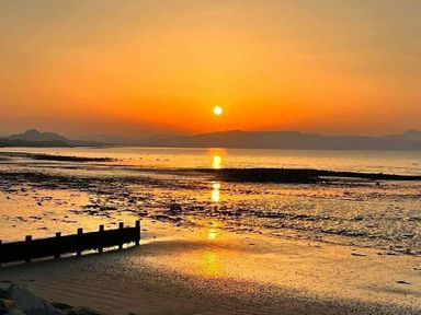 a sunset over the sea with reflections on the water and a shoreline at Hafan y Mor Haven - Holiday Accommodation 11370 in Pwllheli