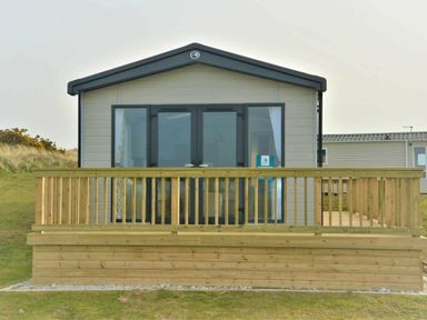 a wooden deck in front of a holiday home with large windows at Perran Sands - Holiday Accommodation 12174, Perranporth
