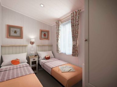 a bedroom with two single beds, framed artwork on the walls, and a window with floral curtains at Perran Sands - Holiday Accommodation 12174, Perranporth