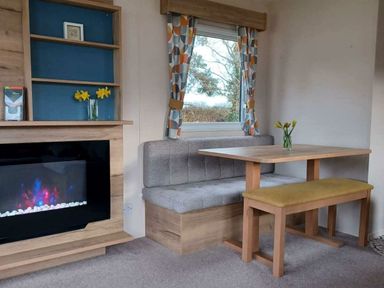 a dining area with a table and bench seating near a modern fireplace at Hafan y Mor Haven - Holiday Accommodation 12637 in Pwllheli
