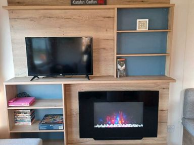 a wooden entertainment unit with a TV and electric fireplace at Hafan y Mor Haven - Holiday Accommodation 12637 in Pwllheli