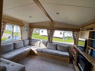 a living room with a sectional sofa and windows at Hafan y Mor Haven - Holiday Accommodation 12637 Pwllheli