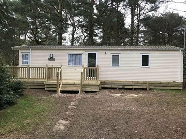 a holiday home with a wooden deck surrounded by trees at Kelling Heath Holiday Park - Holiday Accommodation 13133 in Holt