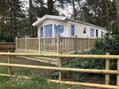 a holiday home with a deck and trees surrounding at Kelling Heath Holiday Park - Holiday Accommodation 13133 in Holt