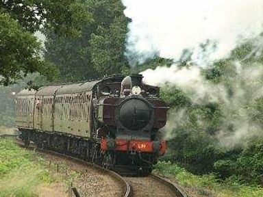 a steam train traveling on a curved railway track surrounded by trees at Kelling Heath Holiday Park - Holiday Accommodation 13133, Holt