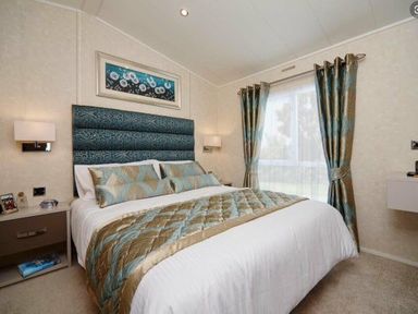 a bedroom with a large bed, decorative headboard, curtains, and side tables at Ocean Edge Leisure Park - Holiday Accommodation 1317, Heysham