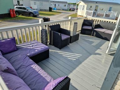 a patio area with wicker furniture and purple cushions at Ocean Edge Leisure Park - Holiday Accommodation 1317, Heysham