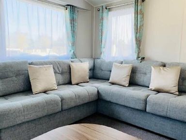 a gray sectional sofa with pillows and windows covered with curtain at Butlins Minehead - Holiday Accommodation 13288 Minehead