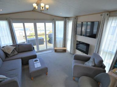 a living room with a sofa, armchair, coffee table, television, and large windows at Perran Sands - Holiday Accommodation 15012, Perranporth