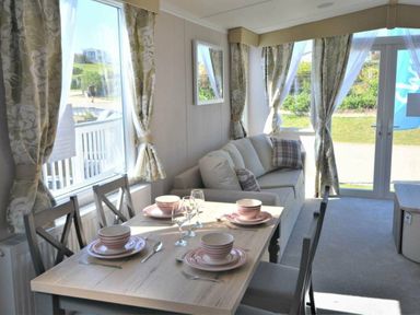 a dining area with a table set for four and a sofa near large windows at Perran Sands - Holiday Accommodation 15554 Perranporth