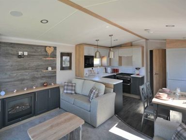 a living room with a sofa, coffee table, and kitchen area at Perran Sands - Holiday Accommodation 15554, Perranporth