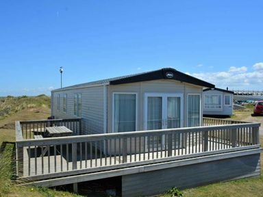 a holiday caravan with a deck and picnic table at Perran Sands - Holiday Accommodation 15598 in Perranporth