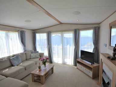 a living room with a sectional sofa, coffee table, television, and large windows at Perran Sands - Holiday Accommodation 15598 in Perranporth