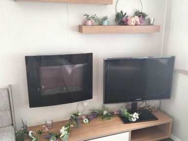 a wall-mounted TV and a separate TV on a unit with floral decorations at Hafan y Mor Haven - Holiday Accommodation 15817 Pwllheli