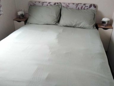 a bed with light green linens and two pillows at Hafan y Mor Haven - Holiday Accommodation 15817, Pwllheli