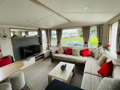 a living room with a sectional sofa, TV, and windows at Unity Holiday Resort - Holiday Accommodation 15970 Brean Sands