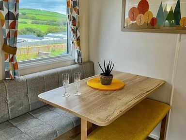 a dining area with a wooden table, gray seating, a potted plant, and decorative artwork at Newquay Bay Resort - Holiday Accommodation 15978, Newquay