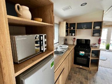a kitchen with wooden shelves, a microwave, a stove, a sink, and various kitchenware at Newquay Bay Resort - Holiday Accommodation 15978, Newquay