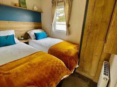 a bedroom with two single beds featuring orange throws and blue cushions at Newquay Bay Resort - Holiday Accommodation 15978, Newquay