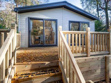 a wooden deck leading to a cabin with large glass doors at Kelling Heath Holiday Park - Holiday Accommodation 16221 in Holt