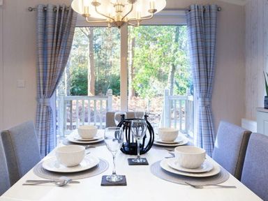 a dining table set with plates and glasses in a room with large windows at Kelling Heath Holiday Park - Holiday Accommodation 16221, Holt