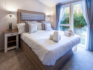 a bedroom with a double bed, bedside tables, and large windows at Kelling Heath Holiday Park - Holiday Accommodation 16221, Holt
