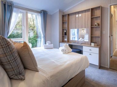 a bedroom with a bed, a desk area, and windows at Kelling Heath Holiday Park - Holiday Accommodation 16221, Holt