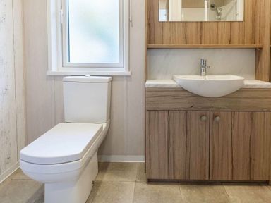 a bathroom with a toilet and a sink with wooden cabinetry at Kelling Heath Holiday Park - Holiday Accommodation 16221 in Holt