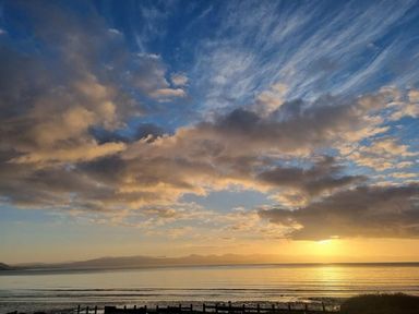 a sunset over a calm sea with clouds and mountains in the background at Hafan y Mor Haven - Holiday Accommodation 16251 in Pwllheli