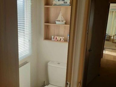 a bathroom with a toilet and shelf displaying decorative items at Unity Holiday Resort - Holiday Accommodation 16507, Brean, Somerset, United Kingdom