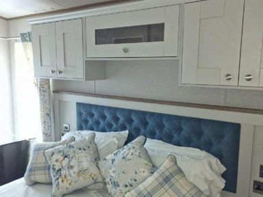 a bedroom featuring a blue upholstered headboard and decorative pillows at Lakeland Leisure Park - Holiday Accommodation 16942 in Flookburgh