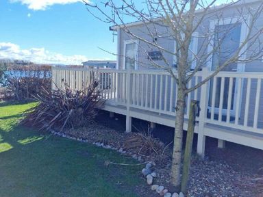 a cabin with a deck and a tree beside it at Lakeland Leisure Park - Holiday Accommodation 16942 Flookburgh