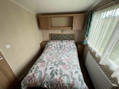 a bedroom with a double bed covered in floral bedding and a window at Hafan y Mor Haven - Holiday Accommodation 17436 Pwllheli