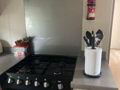 a kitchen countertop with a gas stove, utensil holder, paper towel dispenser, and fire extinguisher at Breydon Water Holiday Park - Holiday Accommodation 18490 in Great Yarmouth