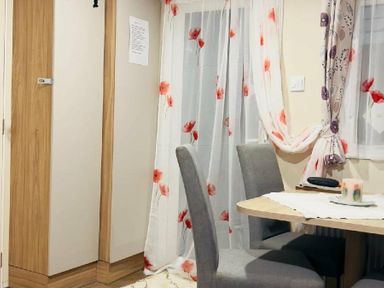 a dining area with a table, chairs, and floral curtains at Breydon Water Holiday Park - Holiday Accommodation 18490, Great Yarmouth