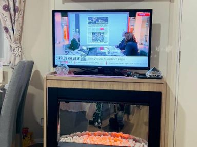 a television displaying news content on a wooden unit with a modern electric fireplace at Breydon Water Holiday Park - Holiday Accommodation 18490, Great Yarmouth