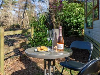 a table with a bottle of rosé wine, two glasses, and cookies at Kelling Heath Holiday Park - Holiday Accommodation 18663, Holt