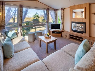 a living room with a sofa, coffee table, TV, and large windows at Kelling Heath Holiday Park - Holiday Accommodation 18663 in Holt