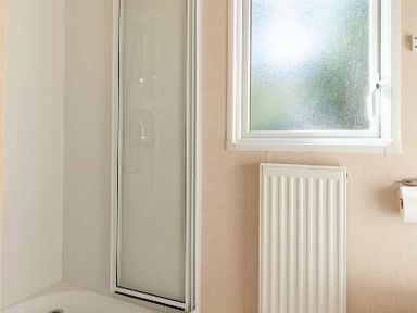 a bathroom with a shower unit, window, radiator, and toilet paper holder at Kelling Heath Holiday Park - Holiday Accommodation 18663 in Holt