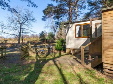 a wooden cabin with a small patio and chairs outside at Kelling Heath Holiday Park - Holiday Accommodation 18663, Holt