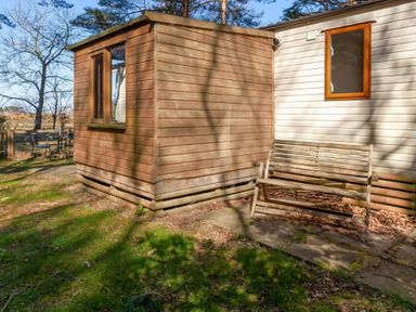a wooden cabin next to a light-colored building with a bench outside at Kelling Heath Holiday Park - Holiday Accommodation 18663 in Holt