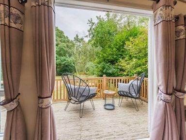a deck with two chairs and a table overlooking greenery at Kelling Heath Holiday Park - Holiday Accommodation 18664, Holt
