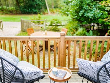 a deck with two chairs and a table overlooking a garden area with a circular wooden table and chairs at Kelling Heath Holiday Park - Holiday Accommodation 18664 in Holt
