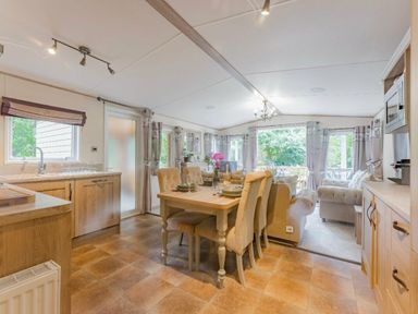 a dining area with a table and chairs, a kitchen area with cabinets, and large windows at Kelling Heath Holiday Park - Holiday Accommodation 18664, Holt