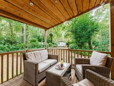 a wooden porch with seating and a table overlooking a forested area at Kelling Heath Holiday Park - Holiday Accommodation 18691, Holt