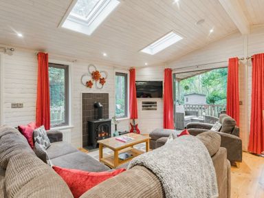 a living room with a stove, large windows, and red curtains at Kelling Heath Holiday Park - Holiday Accommodation 18691 in Holt